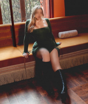 Blonde girl in a green velvet dress sitting on a long couch
