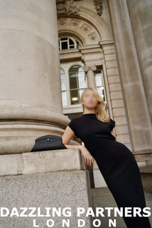 Confident young blond girl in a black dress leaning against an impressive column