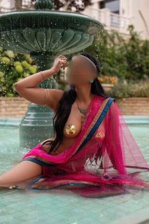 Exotic brunette scantily dressed and sitting in a neo classical fountain