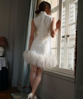 Slim brunette in a stylish white dress at a window looking out