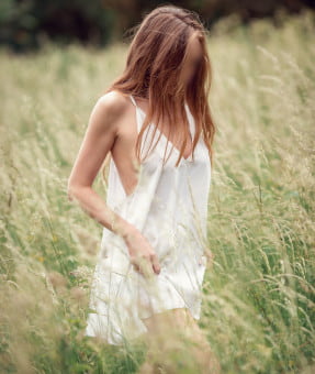 Slender blonde in a white summer dress walking amongst the long grass