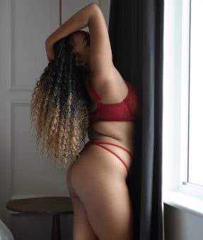 Busty black girl by a window holding her curly locks up