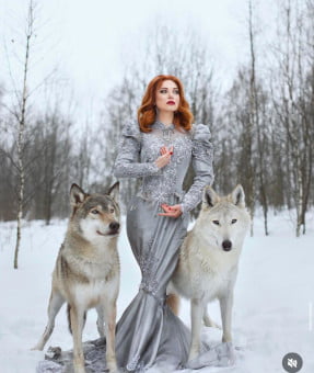 Striking photo of a redhead holding two huskies on leashes in a snow covered forest