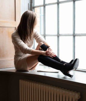 An English petite brunette woman sitting on a window sill looking out of the window