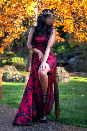 Brunette woman in a park wearing a long pink and black flower pattern dress