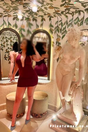Young sexy ebony girl ina red dress standing next to a Greek statue